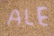 The inscription of ale with malt grains on a lilac textile background. Craft beer brewing from grain barley malt in process. Ale