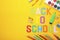 Inscription Back To School with school supplies on yellow background. Colorful letters