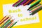 The inscription - back to school, on a sheet of white paper surrounded by colored pencils, markers, paints on a bright yellow back