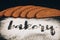 Inscription bakery on white wheat flour scattered Sliced rye bread on dark background
