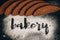 Inscription bakery on white wheat flour scattered Sliced rye bread on dark background