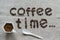 Inscription Coffee Time of a roasted coffee beans on a grey canvas, white porcelain cup of coffee, crema, white porcelain spoon at
