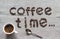 Inscription Coffee Time of a roasted coffee beans on a grey canvas, white porcelain cup of coffee and silver spoon