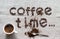 Inscription Coffee Time of a roasted coffee beans on a grey canvas, white porcelain cup of coffee and silver spoon, scattered