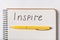 Inscription in copybook INSPIRE. Close up Notepad and pen on white background