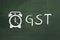 Inscription GST and alarm clock drawn on green chalkboard