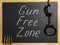 Inscription Gun Free Zone in chalk, handcuffs and cartridges on a school blackboard