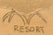 Inscription by hand RESORT in the beach sand in the surf line. Abstract.
