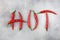 The inscription HOT is laid out from pods of red hot chili peppers on an abstract gray background