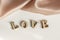 The inscription Love is made of wooden letters, on a background of pink draped silk fabric