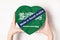 Inscription Made in Saudi Arabia the flag of Saudi Arabia. Female hands holding a heart shaped box. White background