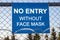 The inscription `NO ENTRY without face mask` on a blue plate