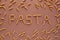 Inscription PASTA of brown pasta in the form of tubes on a brown background