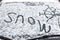 The inscription snow, on the front windshield of the car, covered with snow