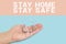 Inscription STAY SAFE and STAY HOME with house in hand palm on blue background
