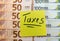 Inscription `taxes` on a yellow sticker on a euro background. Tax concept.