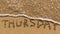 Inscription THURSDAY on a gentle beach sand with the soft wave