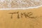 The inscription `time` on the sea sand with the incoming wave. Sandy beach with waves.