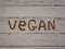 Inscription `Vegan` made from hazelnuts and almonds nuts on a white wooden table top view.