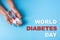 Inscription world diabetes day and blue ribbon awareness with red blood drop in woman hands on a blue background