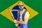 An insecure clown holds a bat in his hands against the background of the flag of Brazil