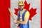 An insecure clown holds a bat in his hands against the background of the flag of Canada