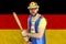 An insecure clown holds a bat in his hands against the background of the flag of Germany