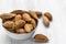 Inshell almonds lie in a white glass cup on a white wooden surface