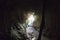 Inside the gloomy cave with damp stone walls and dry grass ceiling supported with stick, the floor has stones and water. Empty