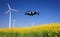Inspection drone with eolian turbines behind. Rapeseed field in bloom. Renewable energy