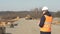 An inspector in a signal vest and a white helmet with black glasses makes notes in his folder on the quality of the road