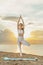 Inspirational beautiful girl practices yoga at dawn on seashore. Woman in tree pose Vrikshasana, sea background