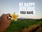 Inspirational quote - Be happy with what you have. With hand holding a flower on rural mountain view over the field.