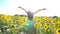 Inspired girl standing among sunflowers field and raising hands. Woman enjoying freedom or beautiful environment. Scenic