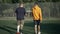 Inspired male mature amputee and teenage boy walking in slow motion on sports field talking. Back view portrait