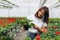 Inspired smiling young woman florist holding flowers of begonia in greenhouse. Female gardener working with plants