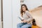 Inspired white young woman in beige shirt sitting on table in kitchen with newspaper. Indoor photo of ecstatic curly