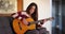 Inspired young Latina woman composing song on acoustic guitar at home