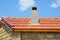 Installing chimney on house construction with red clay roof and limestone wall