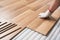 Installing laminated floor, detail on man hand in white glove fitting wooden tile, over white foam base layer