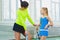 Instructor or coach teaching child how to play tennis on a court indoor