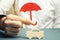 An insurance agent is holding a red umbrella over a miniature wooden car. Auto insurance concept. Vehicle protection. Insurance