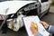 Insurance agent holds clipboard and ballpoint pen closeup and wrecked car in background