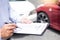 Insurance agent writing on clipboard while examining car after accident claim being assessed and processed