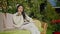 Intelligent beautiful young Asian woman recording voice mail sitting on couch in sunny garden outdoors. Portrait of