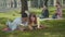 Intelligent young boy and girl in eyeglasses lying on green lawn and reading books as loving couple playing ukulele at