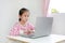 Intend asian little child sitting at desk and using laptop at home