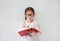 Intend little Asian girl wearing eyeglasses holding and writes in a notebook with pencil on white background