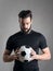 Intense portrait of football player holding and looking at the ball focused over gray studio background