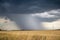 An intense shaft of rain and hail descends to the ground from a dark storm cloud.